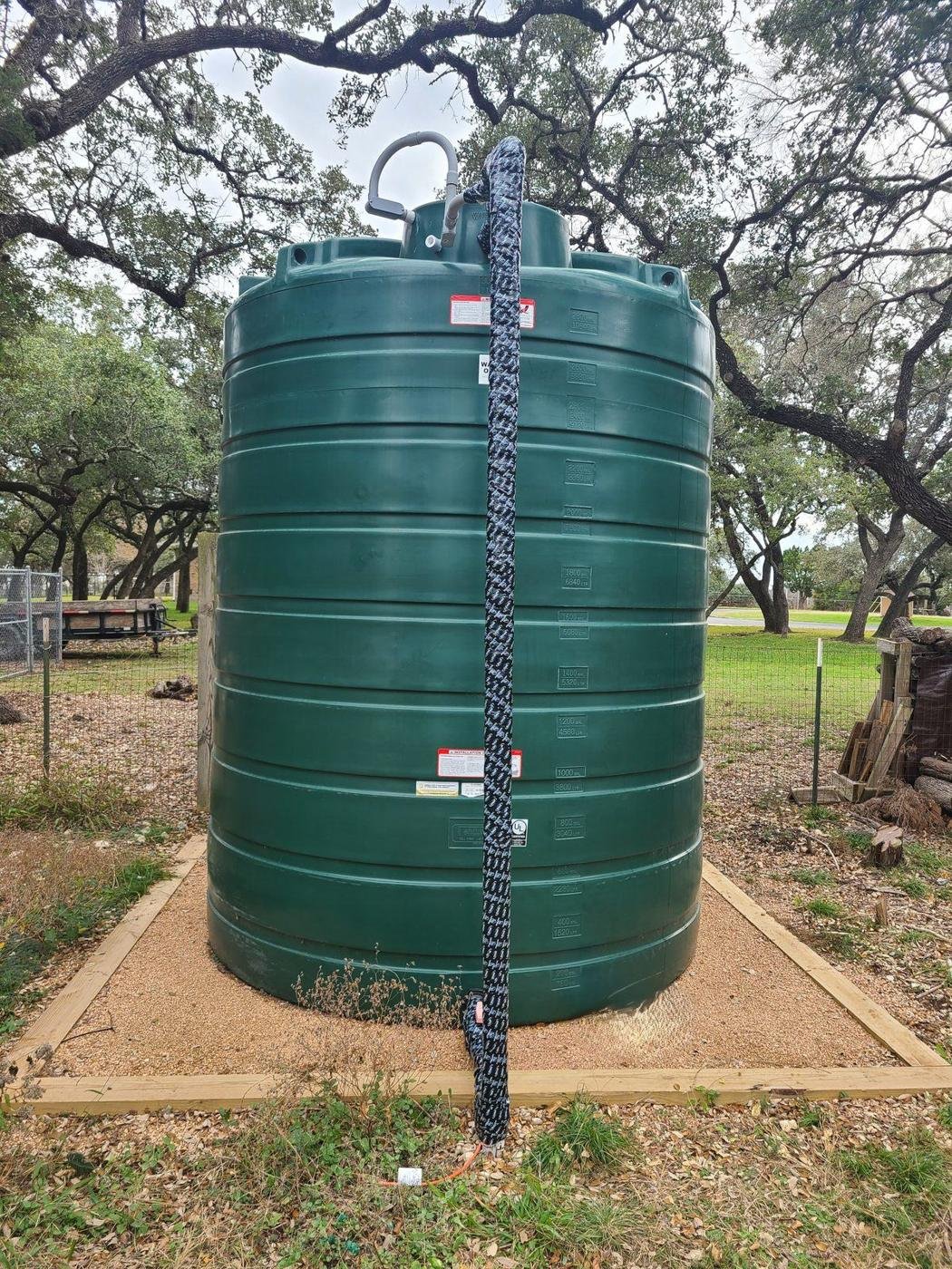 3,000-gallon green water storage tank on a crushed granite pad under live oaks in Central Texas