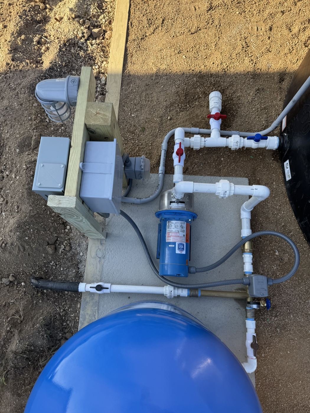 Overhead view of a booster pump, valve manifold, pressure switch and low-water alert light on a concrete equipment slab