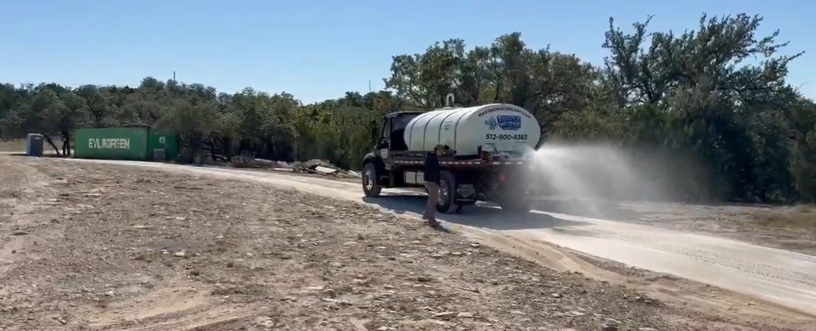 Dust control water truck spraying a construction site access road in the Austin area