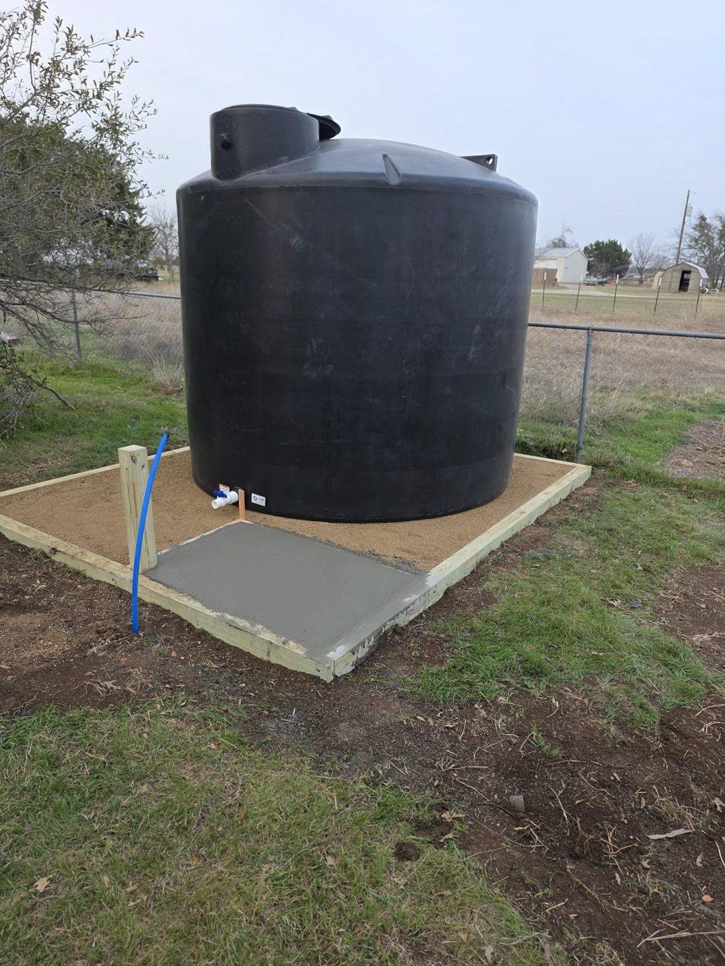 Water storage tank set on a framed crushed granite pad with a concrete equipment slab